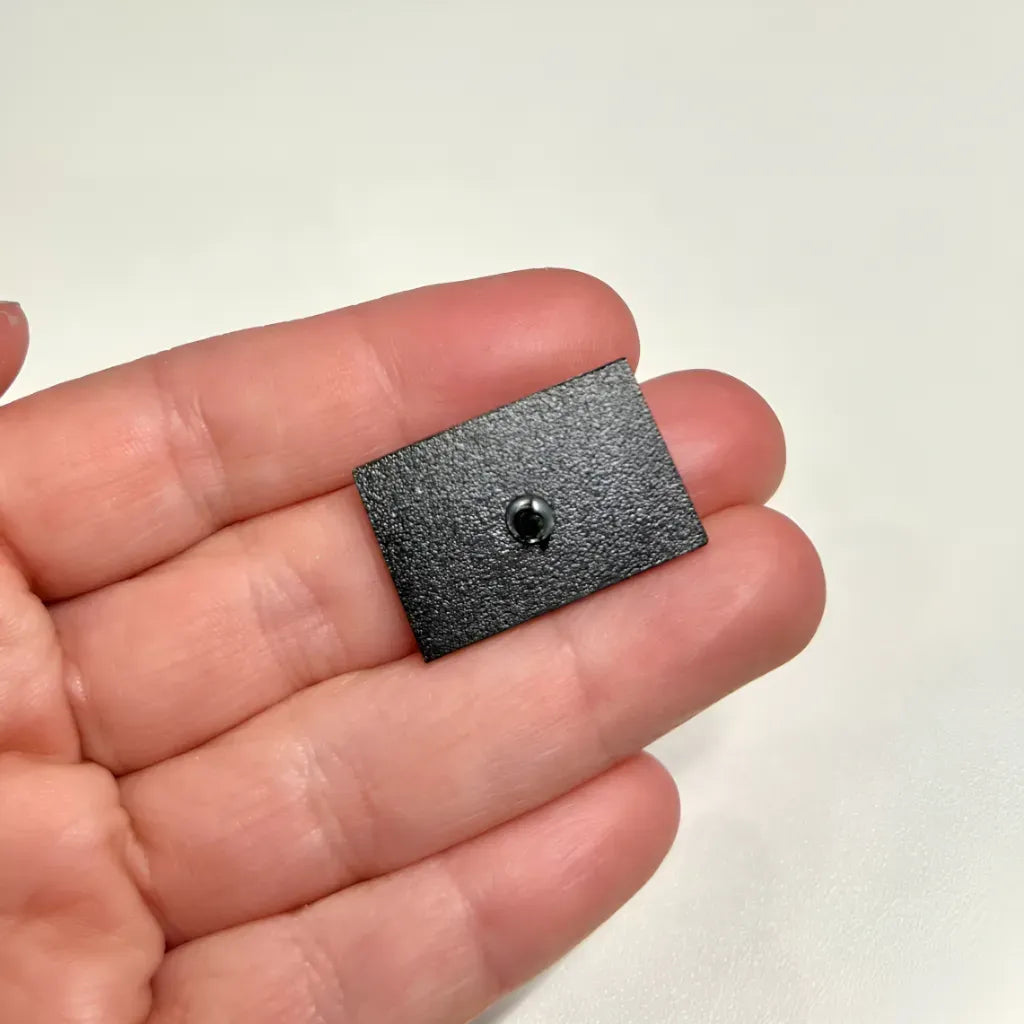 The back of a Progress Pride Flag (with Intersex) Pin held in a person’s palm, showing a metal pin post.