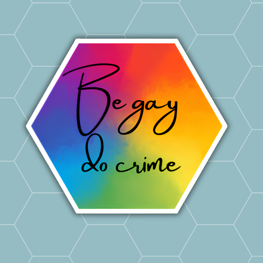 A hexagonal sticker with a white border and a vibrant rainbow gradient background, featuring the text 'Be gay do crime' in black cursive script, set against a light blue-gray hexagonal grid background.