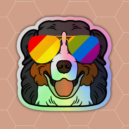 A die-cut sticker featuring a cartoon dog with black fur and rainbow aviator sunglasses, shown on a peach hexagonal background.