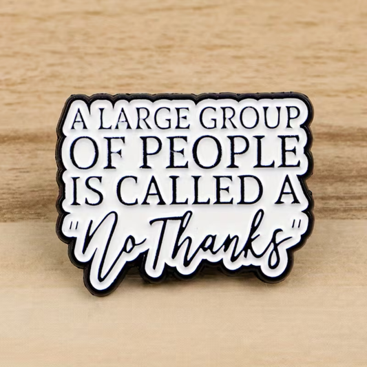 A sign featuring the witty phrase “A large group of people is called a No Thanks” on a white surface with black lettering, set against a wood background. The playful design echoes the style of RainBee Designs LLC’s “A Large Group of People is Called a No Thanks Pin”—perfect for anyone who values personal space.