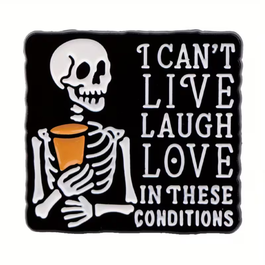 The “I Can’t Live Laugh Love in These Conditions Pin” from RainBee Designs LLC features a cartoon skeleton holding a cup beside the phrase “I can’t live laugh love in these conditions” on a black background, making it an ideal choice for a quirky and funny enamel lapel pin.