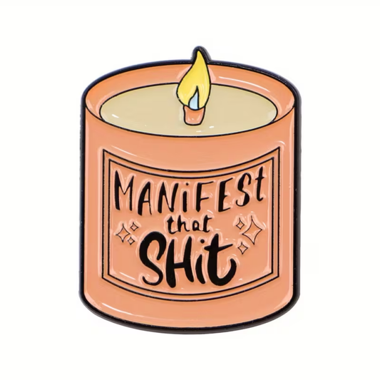Introducing the Manifest That Shit Candle Pin by RainBee Designs LLC: a charming enamel pin depicting a glowing beige candle in an orange holder adorned with sparkles and the words “Manifest That Shit” on its label—an inspirational accessory for anyone who loves positive vibes and manifesting.