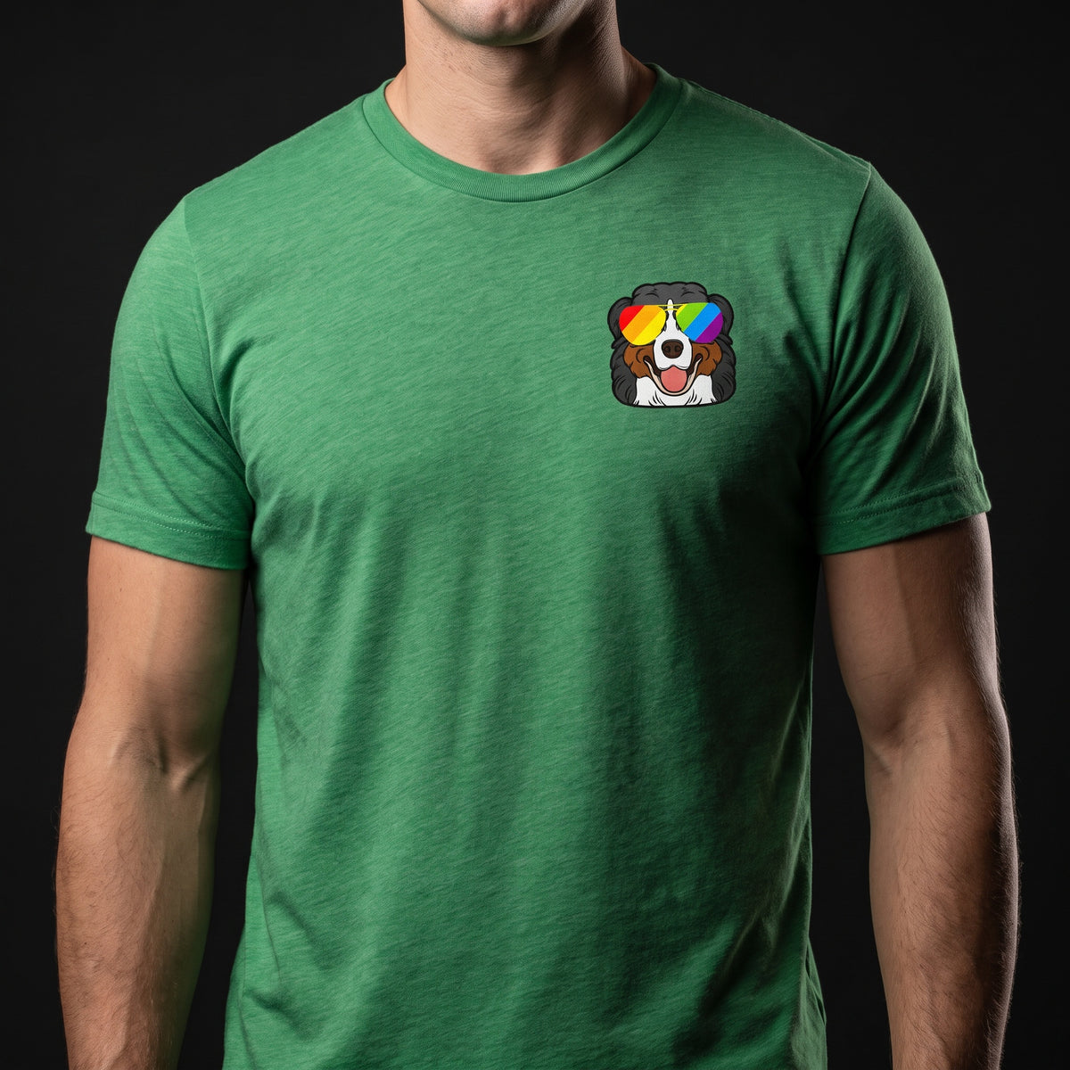 A person wearing the RainBee Designs LLC Berner Pride T-Shirt, which features a small cartoon Bernese Mountain Dog with rainbow sunglasses on the left chest, set against a black background.