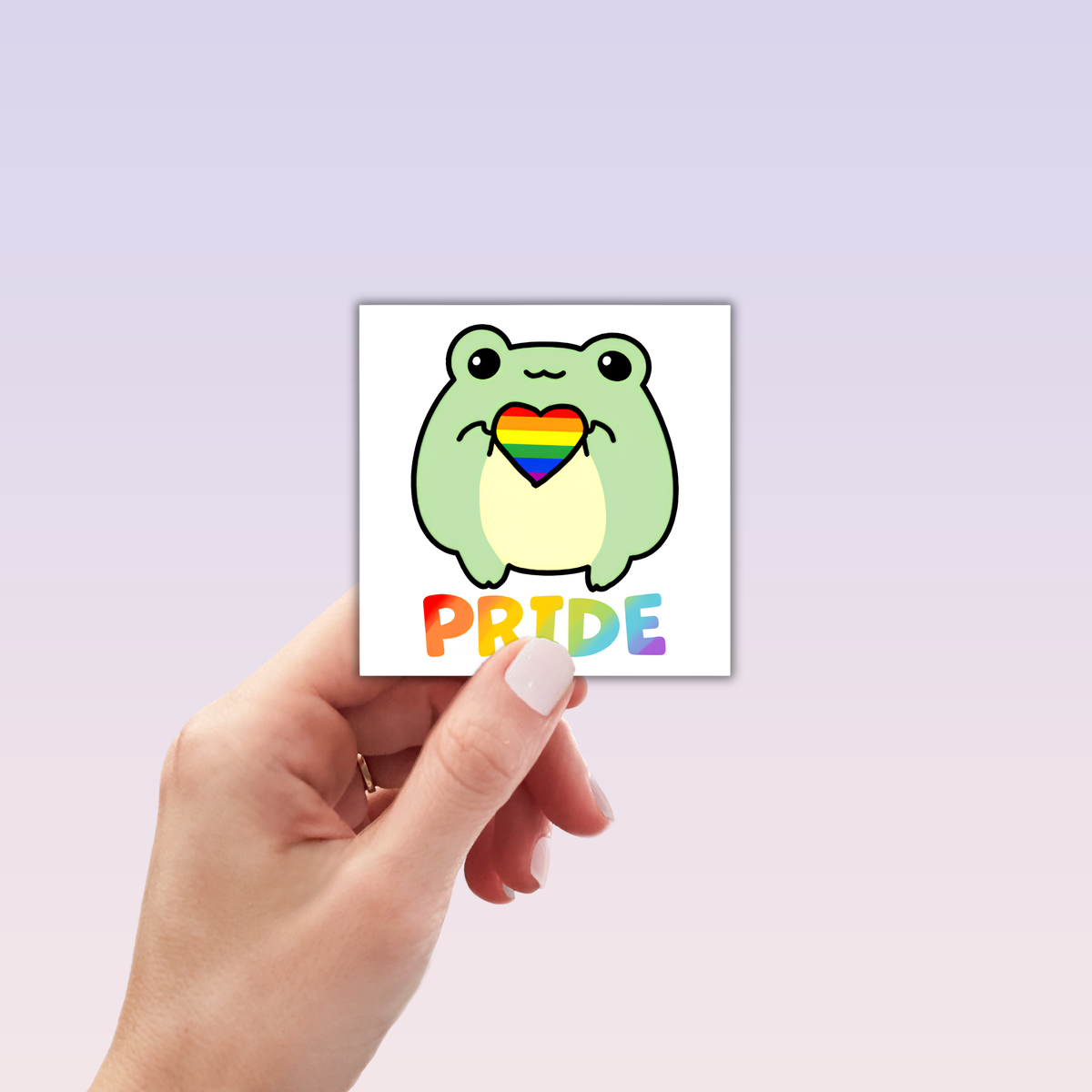 A hand holds the Pride Frog Sticker: a square vinyl matte sticker with a cartoon frog holding a rainbow heart, "PRIDE" in rainbow letters beneath, all set against a soft lavender gradient background.