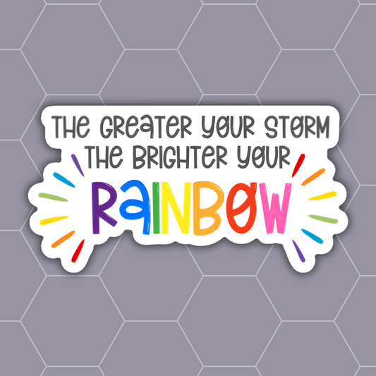 A die-cut vinyl sticker with the motivational quote 'THE GREATER YOUR STORM THE BRIGHTER YOUR RAINBOW' in gray text, featuring a colorful rainbow lettering design on a white background with a gray hexagonal pattern backdrop.