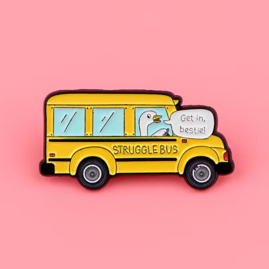 A yellow school bus enamel pin with a cartoon goose driver and a speech bubble that says 'Get in, bestie!' on a solid pink background.