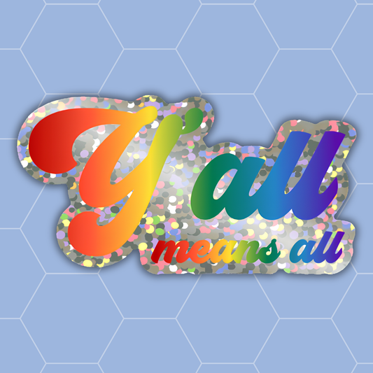A die-cut sticker featuring the phrase 'y'all means all' in a rainbow gradient font over a silver glitter-textured background, shown on a light blue patterned backdrop.