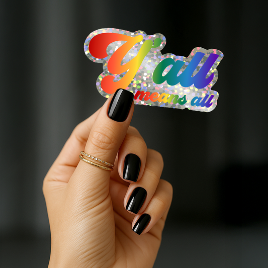 A hand with black nail polish holds the Y'all Means All Sticker by RainBee Designs LLC—a glittery rainbow Pride sticker that shines brightly and celebrates inclusivity. The person, wearing a thin gold ring, displays this vibrant sticker with pride.